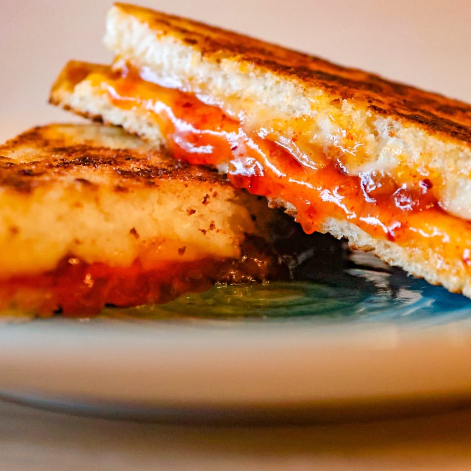 Grilled cheese sandwich with melted cheese and red sauce on a ceramic plate.