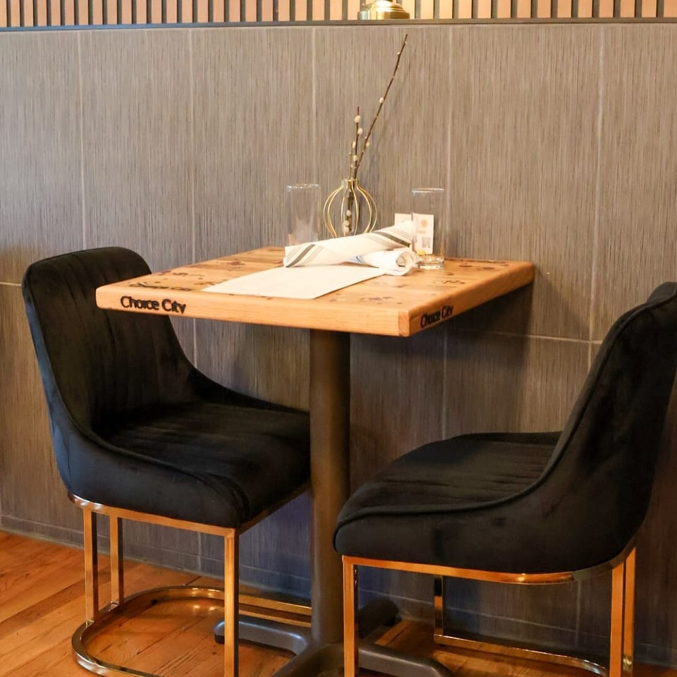 Cozy restaurant table set with folded napkins, glasses, floral centerpiece, and two black upholstered chairs.