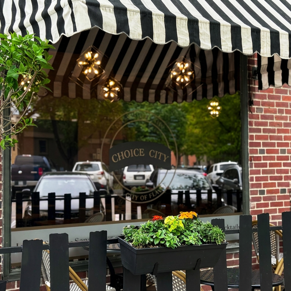 Brick restaurant exterior with black-and-white striped awning, patio seating, planter boxes, and illuminated pendant lights.
