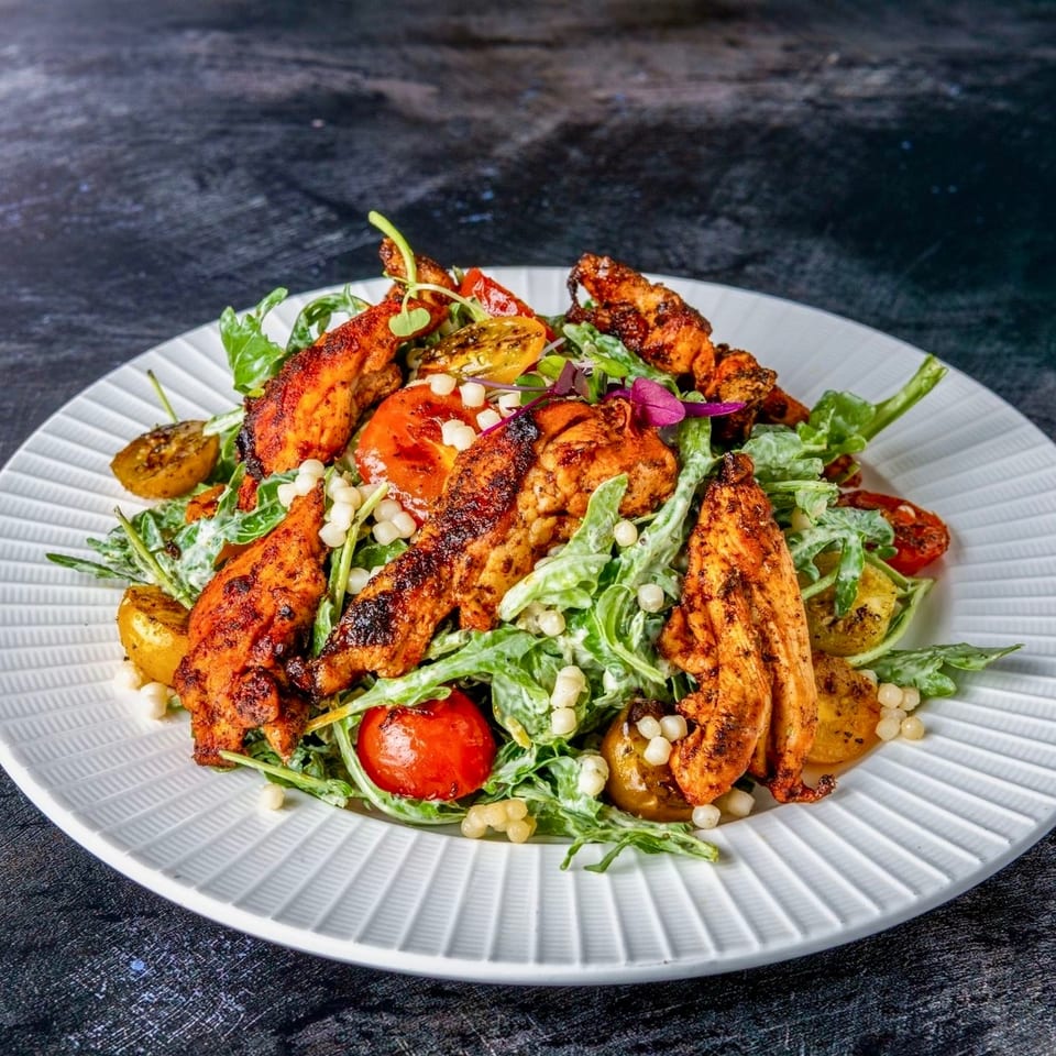 Grilled chicken strips served over a leafy green salad with roasted potatoes, tomatoes, corn, and edible flowers.